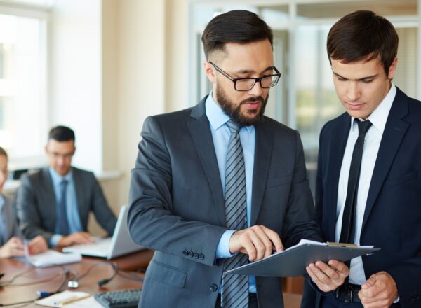 Confident businessman pointing at document while explaining his idea to his partner on background of their colleagues